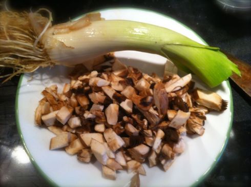Leak (top) waits to be diced on a plate with prepared mushrooms.